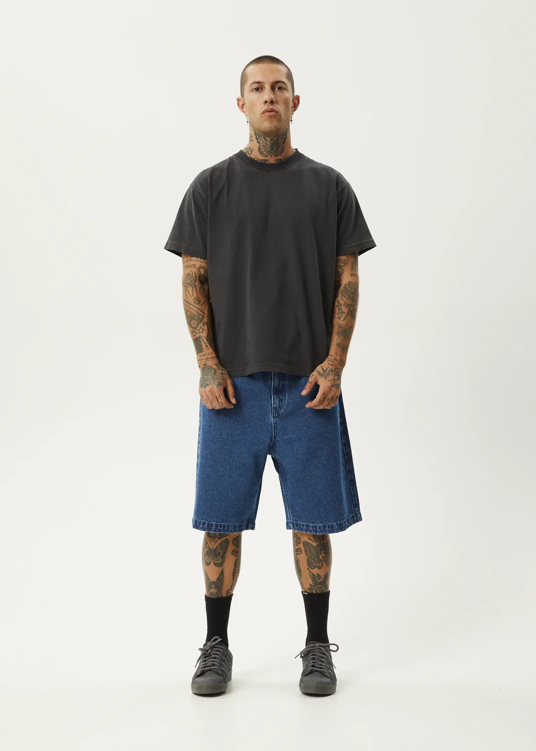 Man wearing a black t-shirt and blue denim shorts on a white background