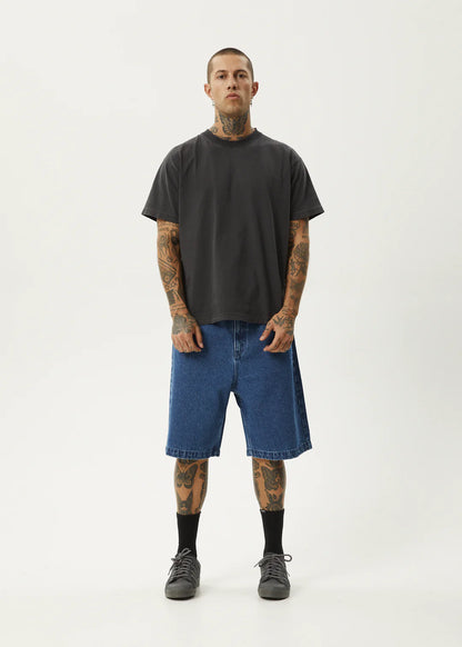 Man wearing a black t-shirt and blue denim shorts on a white background